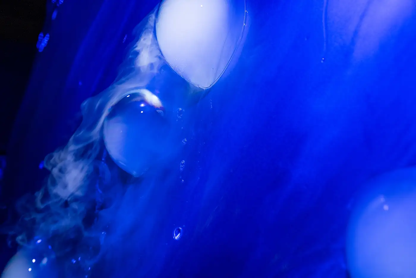 Bubbles and mist drifting across the sculpture under blue light